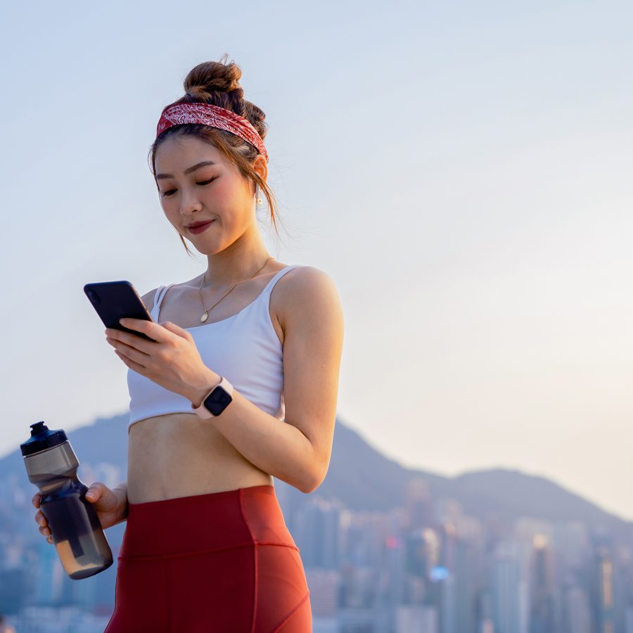 Next to Hong Kong’s harbour, a woman on an evening jog, with a water bottle in hand, looks down and smiles at her phone. 