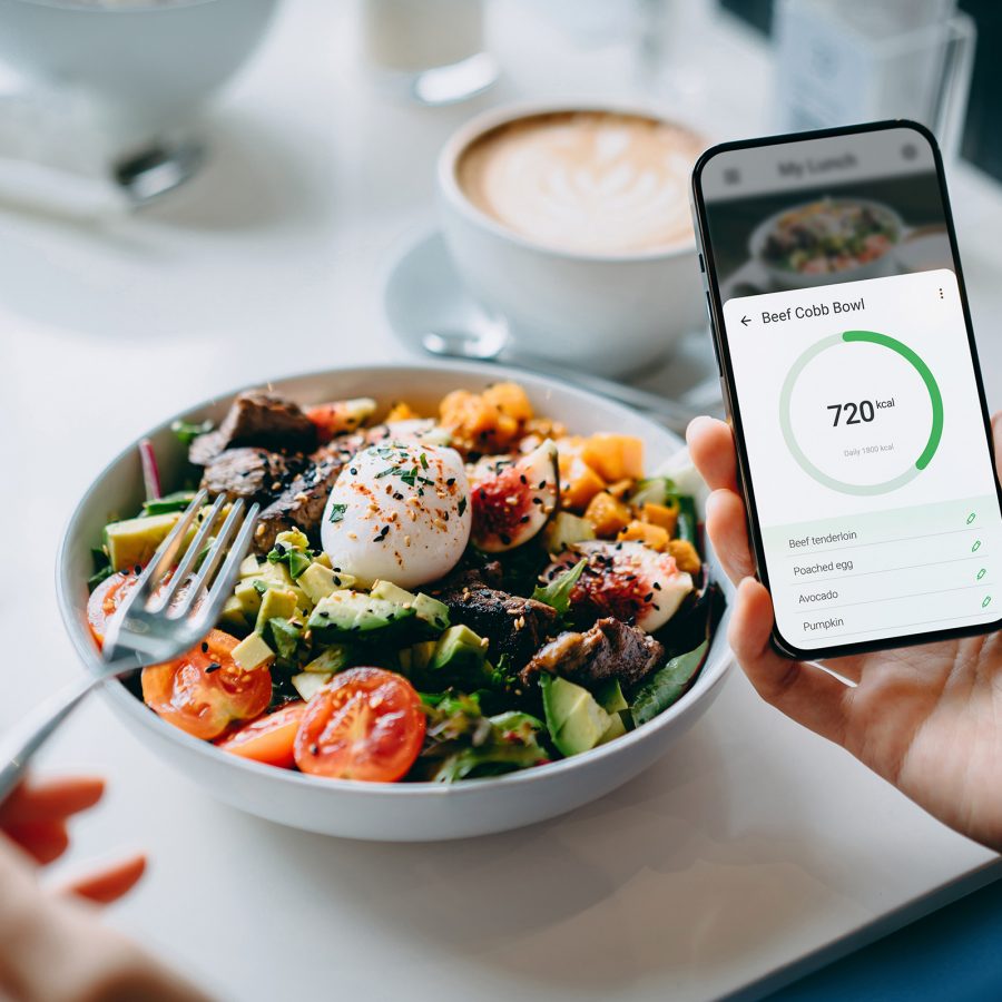 A person getting ready to eat a nutritious salad full of whole foods looks at a nutrient and calorie tracker on their phone. 