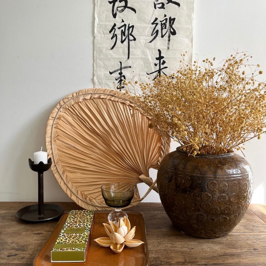 A closeup of various homeware and lifestyle products on a wooden table with Chinese calligraphy on the wall in the background, sold at Lumeun Home in Hong Kong.