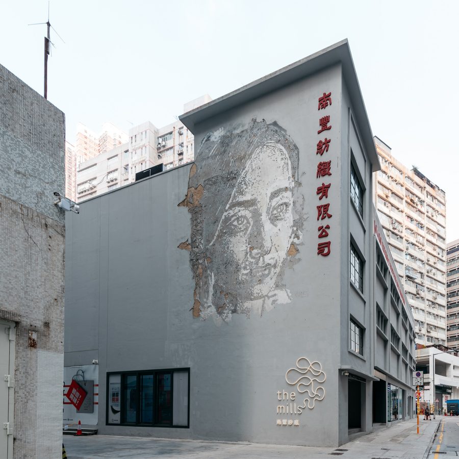 A street view of the exterior of The Mills, featuring a mural of a woman by The Mills Gallery in Tsuen Wan, Hong Kong during daytime.