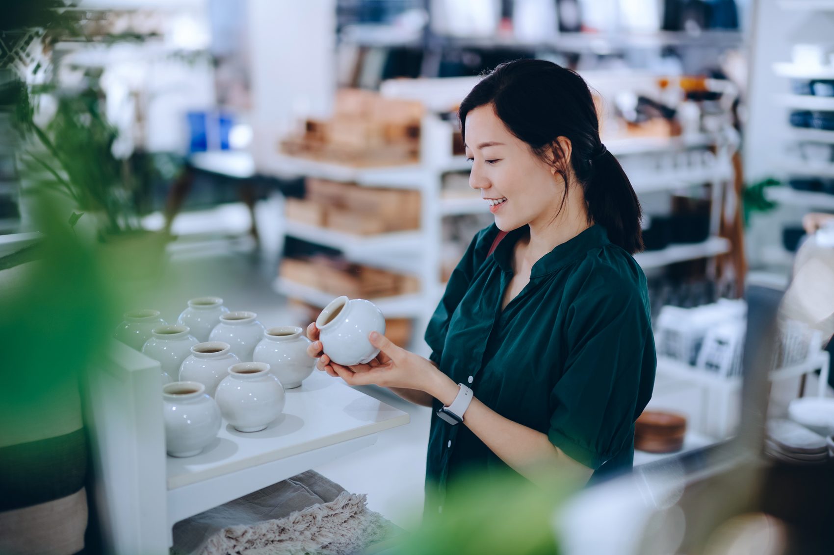  A woman smiling while holding a white ceramic pot in a homeware shop. 