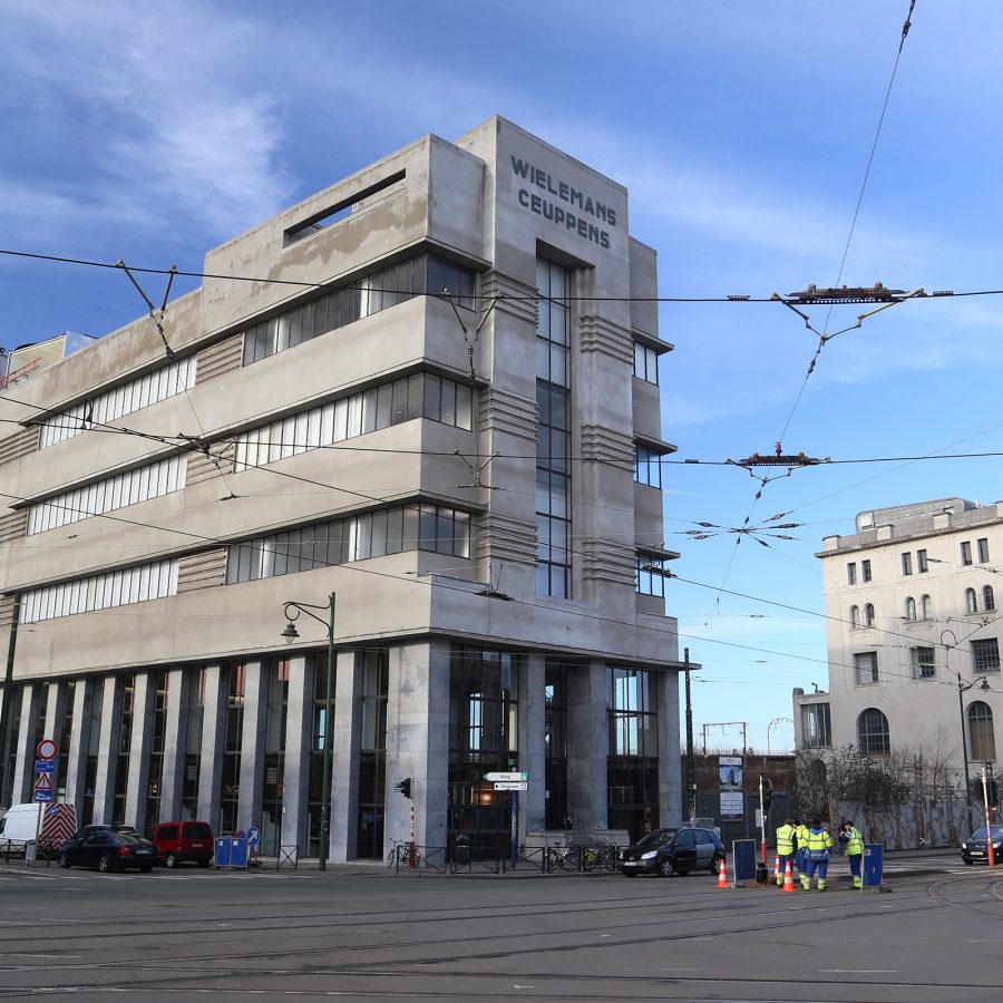 The concrete exterior of Wiels contemporary art centre. Tram lines and cables run in front of it. 