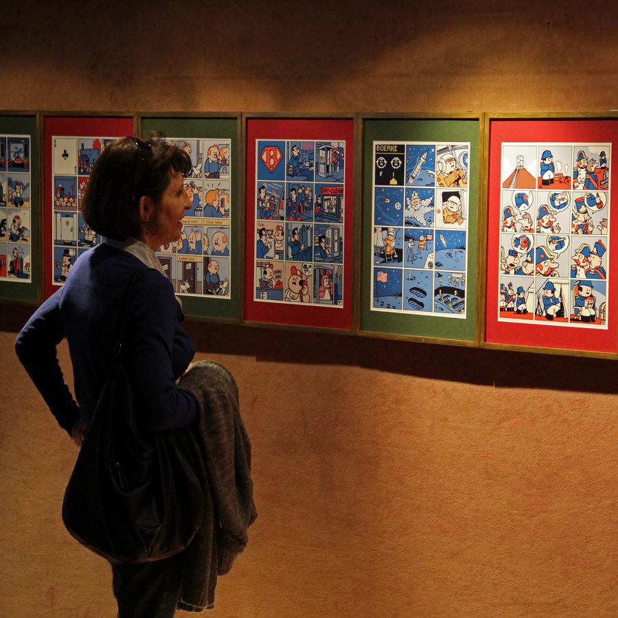 A person views a series of comic strips displayed on a wall.