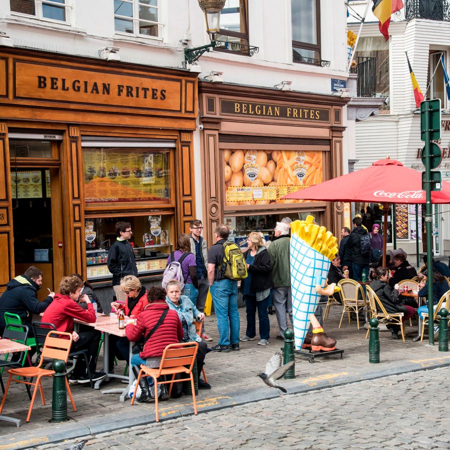 On a street in Brussels, people sit at tables outside eateries selling Belgian frites.
