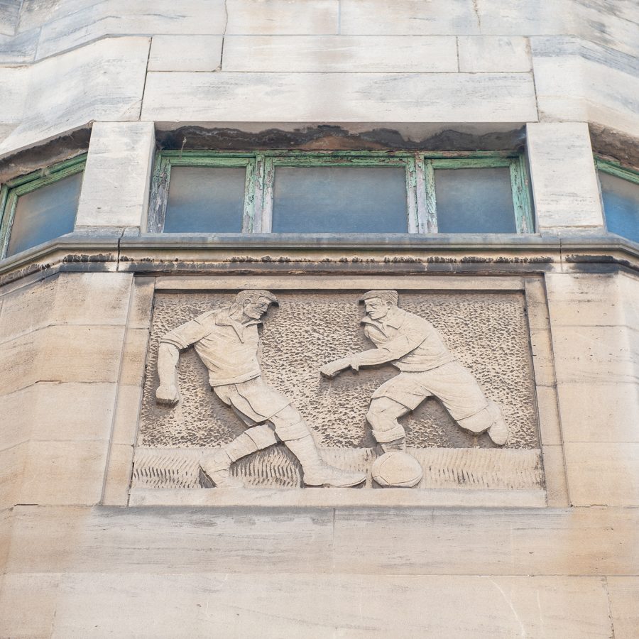 The façade of the Joseph Marien Stadium features a carving of two football players kicking a ball.