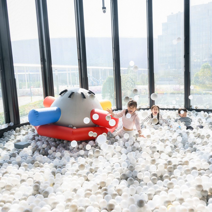 Three smiling children in a ball pit at Joypolis Sports, Hong Kong.