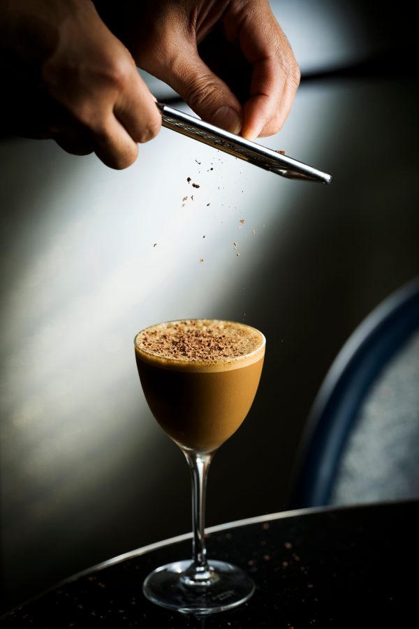 Hands grating chocolate onto a cocktail at Jin Bo Law, the Dorsett Kai Tak, Hong Kong. 