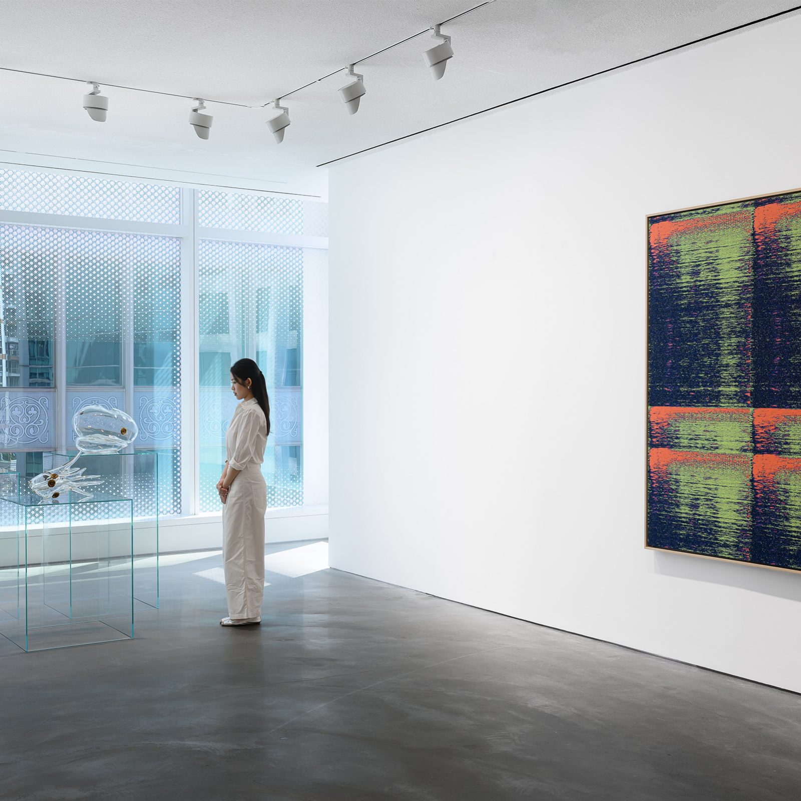 Wide shot of an elegantly-dressed woman standing in a bright, spacious gallery, with a large painted canvas displayed on one wall.