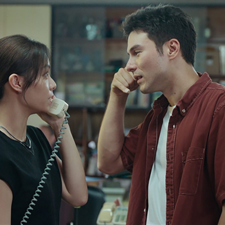 In a scene from TV series The Cleaner, a young woman, Li-ying (Vivian Sung) and man, Chuan (Rhydian Vaughan) stand in an old-fashioned office. Li-ying holds a landline telephone.