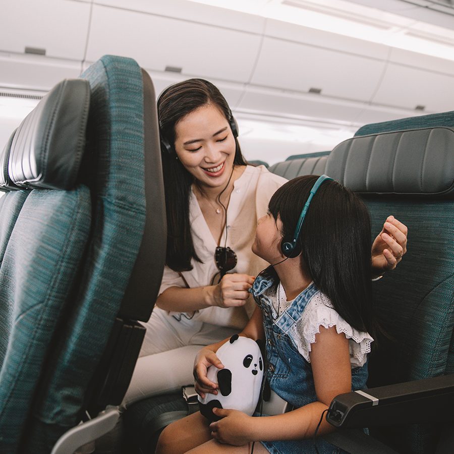 A mother helps her daughter wear a Cathay Pacific headset inside an aircraft. 
