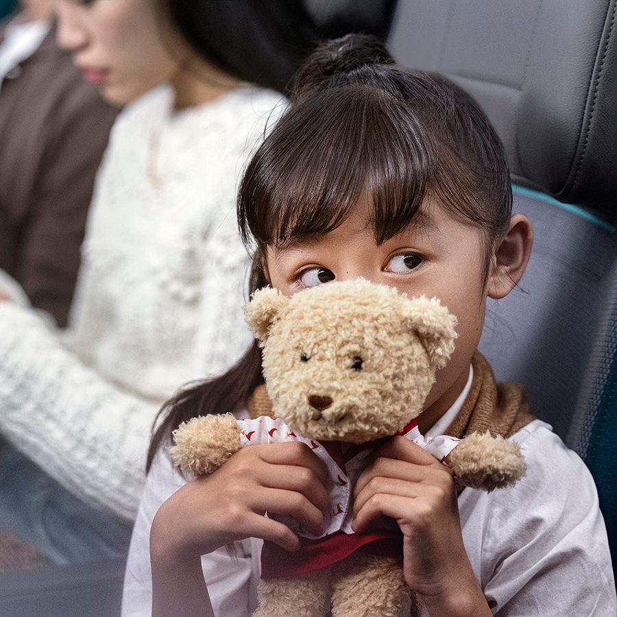 A young girl holding a teddy bear soft toy while sitting in an aircraft.