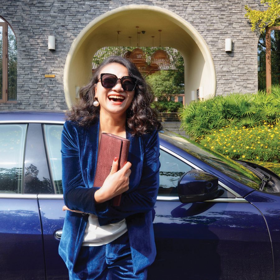 Liz Shi smiling in front of a blue car in the daytime.