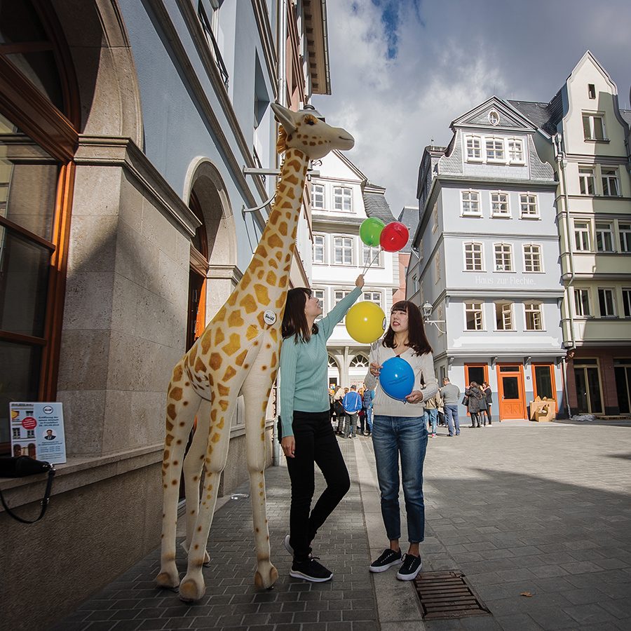 Two women stand outside Steiff and its giraffe statue in Neue Altstadt