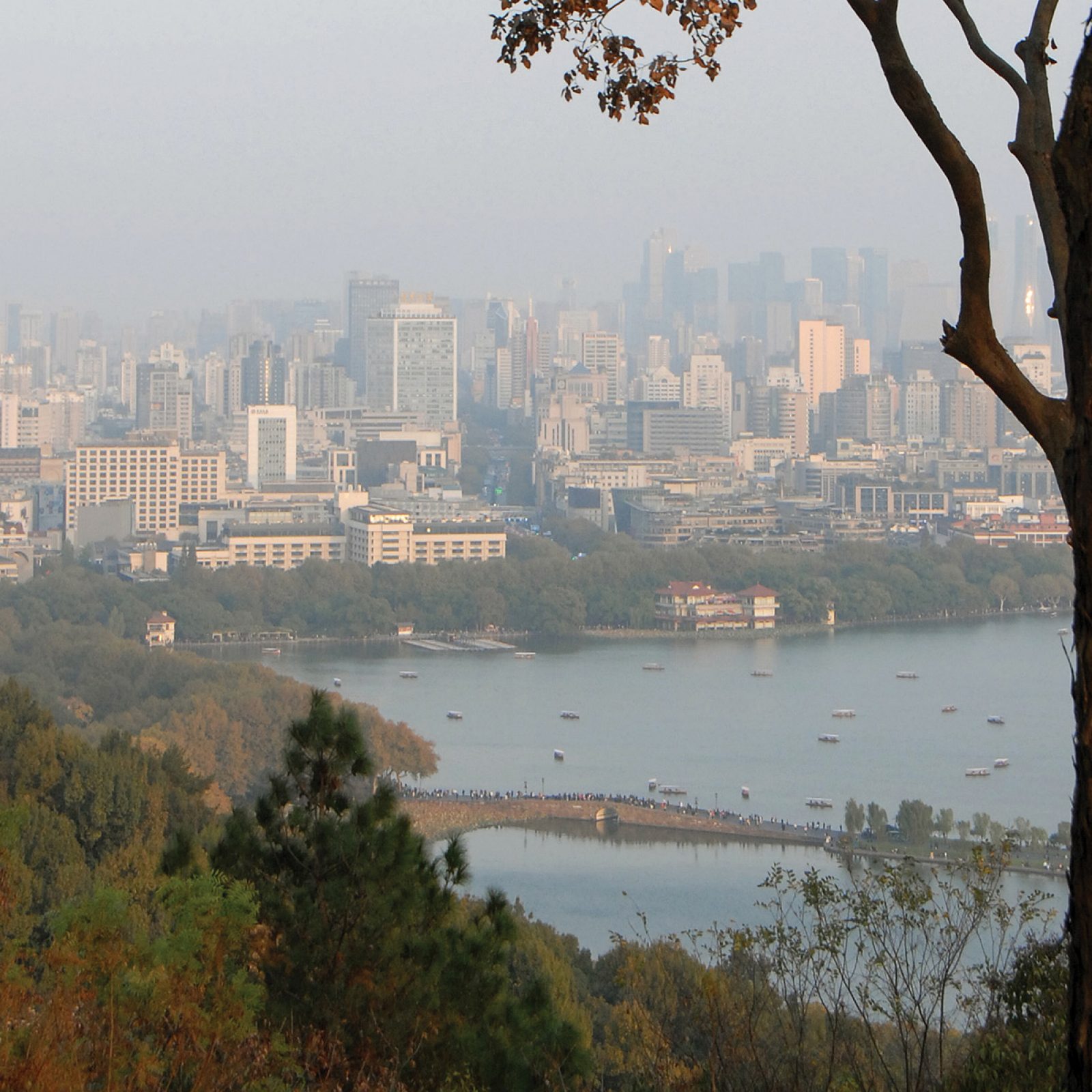 The view from Baoshi Mountain, with trees and West Lake in the foreground and city skyscrapers in the background.