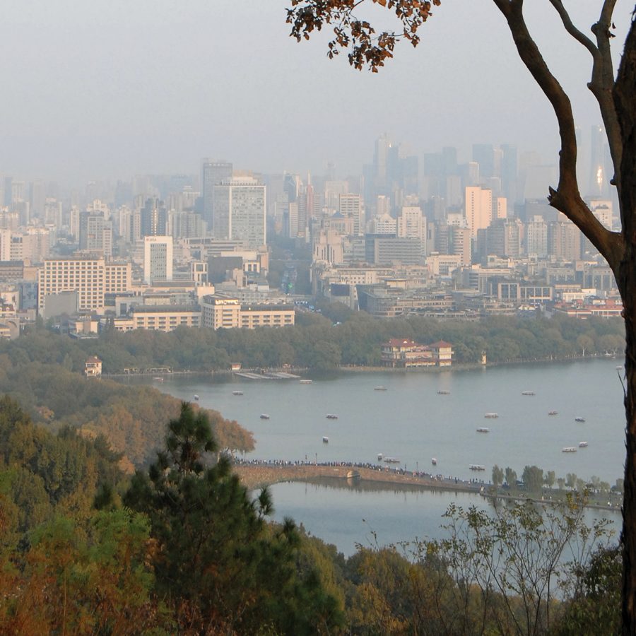 The view from Baoshi Mountain, with trees and West Lake in the foreground and city skyscrapers in the background.