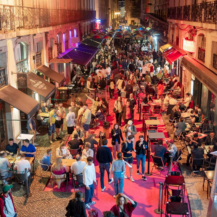  A crowd of people gather at Rua Nova do Carvalho pink street in Lisbon outside restaurants and bars at night.