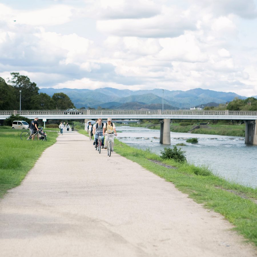 People riding bikes on a path by Kamo River. 