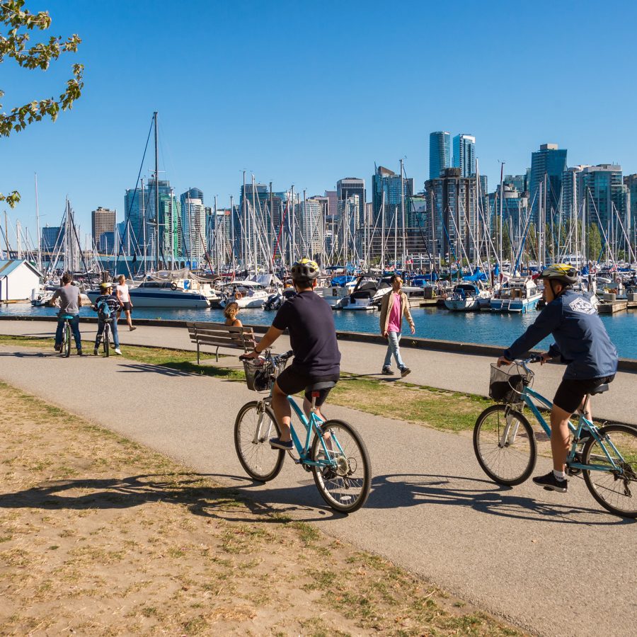 People riding bicycles on a path next to a body of water in Stanley Park.  