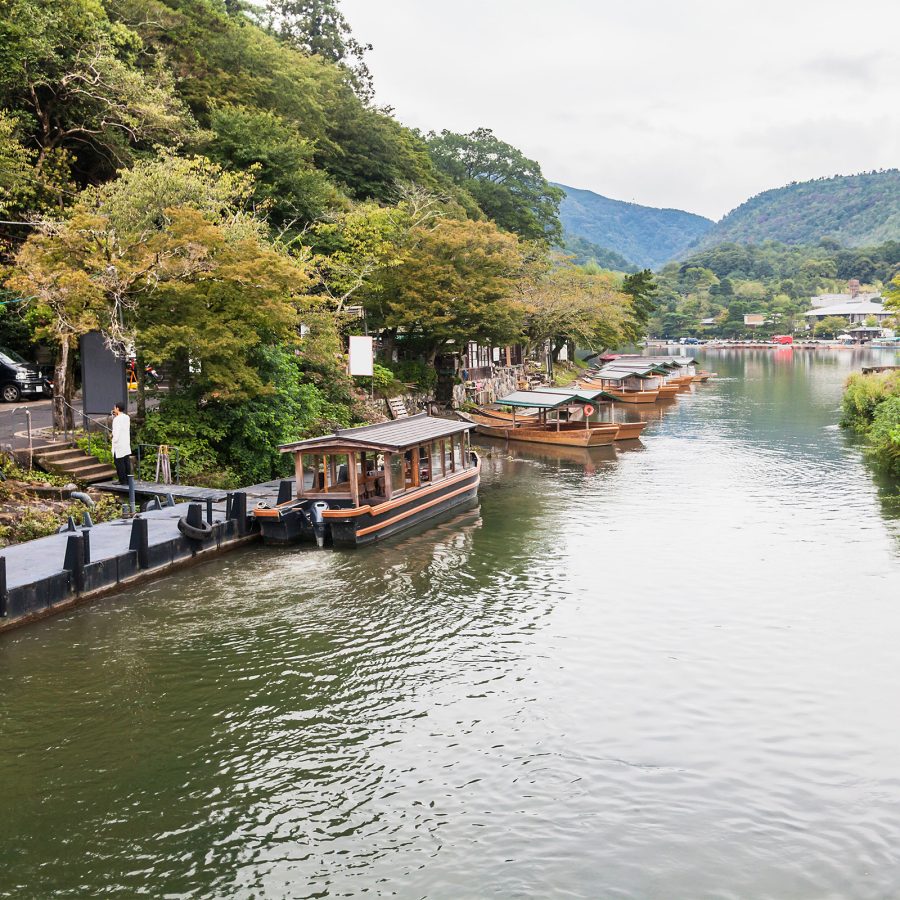 Boats on the tree-lined Kamo River, with mountains in the distance. 