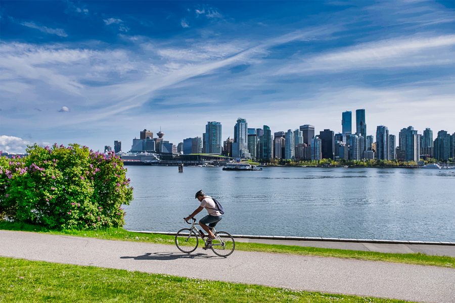 A person riding a bicycle on a path next to a body of water in Stanley Park. 