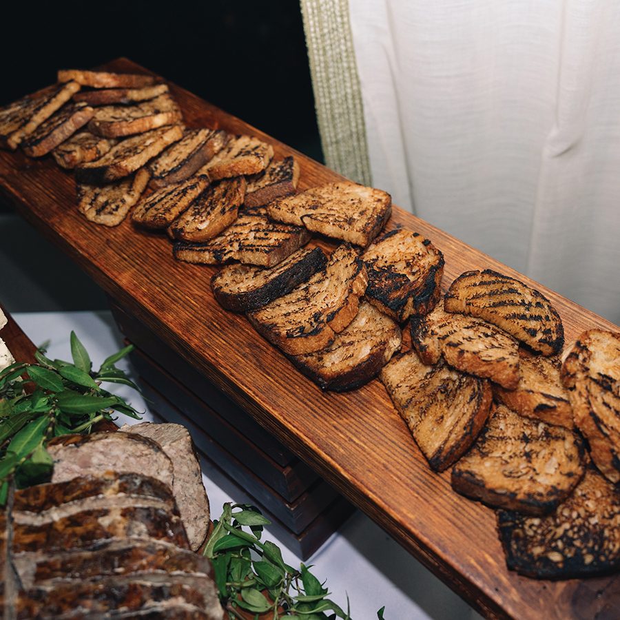 Grilled slices of bread are laid across a long wooden board at at The Rescued Feast 3.0.