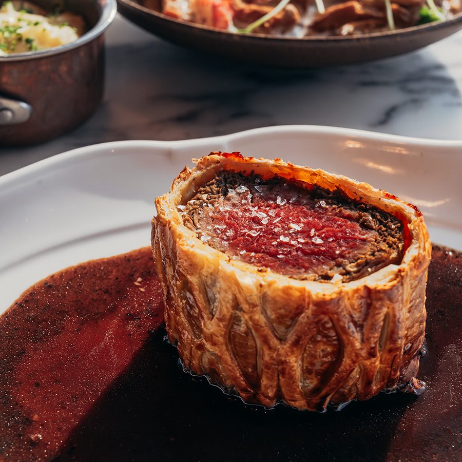 Close up shot of a beef wellington slice surrounded by gravy at ALTO Bar & Grill