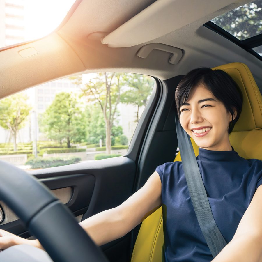A closeup view of an Asian woman in a car, smiling while driving through the city