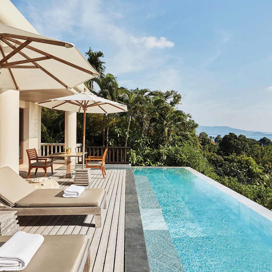 An outdoor view of the private villa and swimming pool during daytime, featuring outdoor lounge chairs and sun umbrellas and a seaview of Phuket’s coast