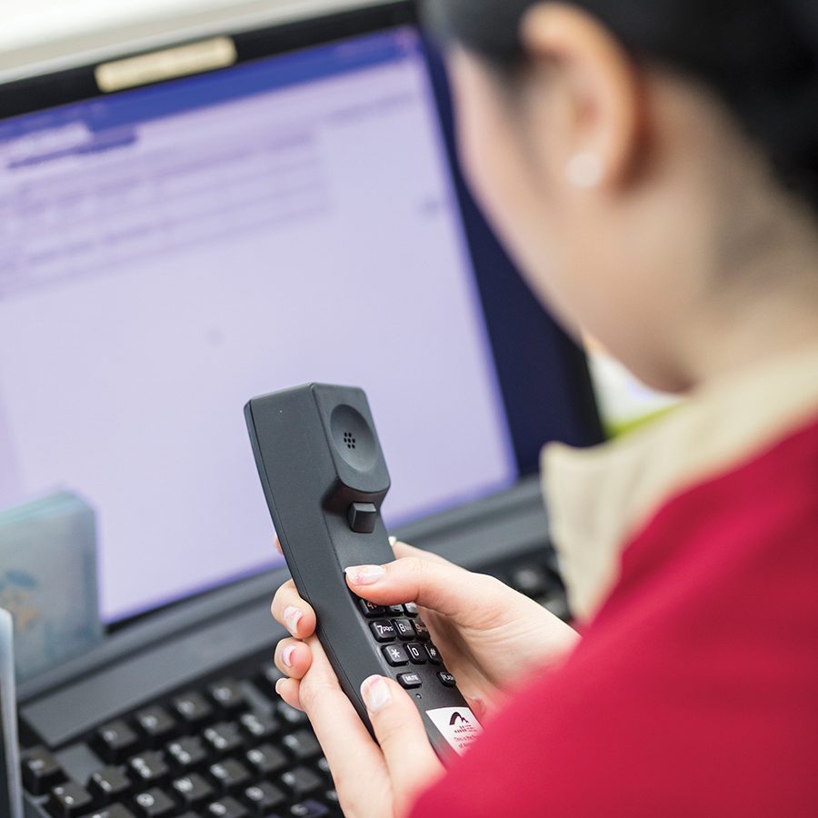 A female member of Cathay Pacific’s ground staff holding a phone while looking at a computer screen.