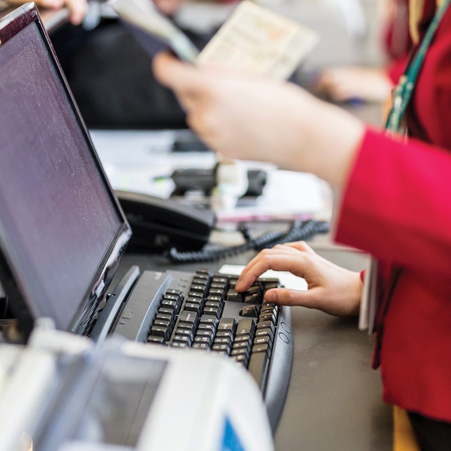 A female member of Cathay Pacific’s ground staff typing at a computer while holding a passport.