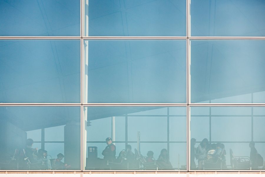 Passengers at an airport reflected in the windows in the daytime.