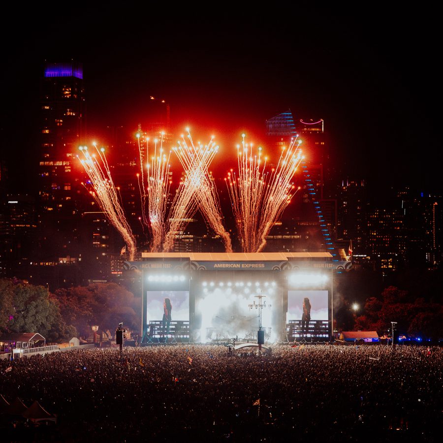 Dua Lipa performing at Austin City Limits at night. Red fireworks explode from the stage. 
