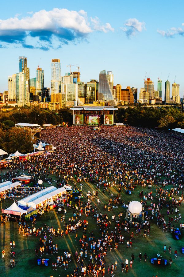 Aerial view of Chappell Roan performing at Austin City Limits to a massive crowd in the daytime. The skyline of Austin is in the background.
