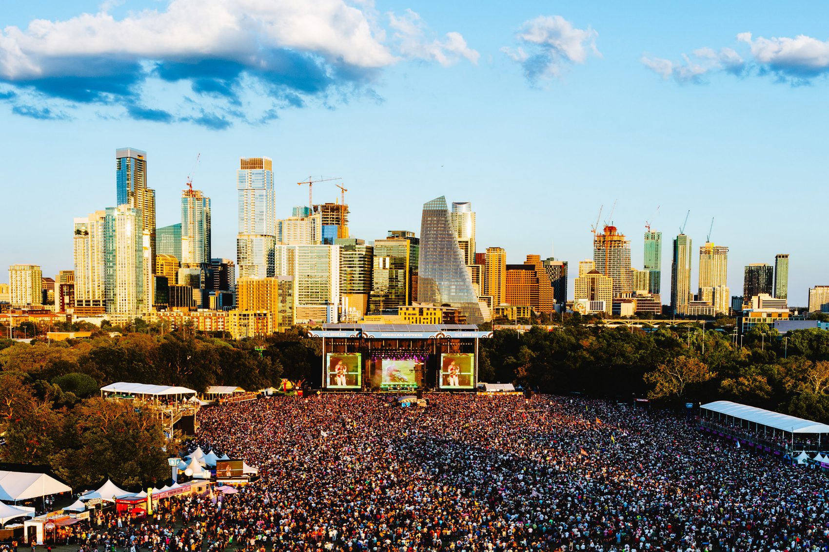 Aerial view of Chappell Roan performing at Austin City Limits to a massive crowd in the daytime. The skyline of Austin is in the background.