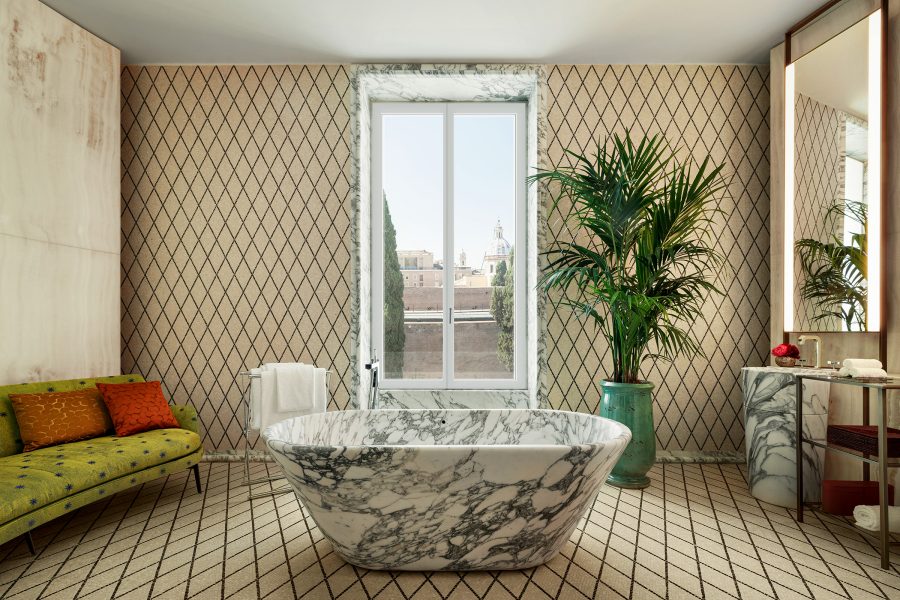 An interior view of a bedroom suite bathroom with marble bathtub and a tall window with city views of Rome at Bulgari Hotel Roma.
