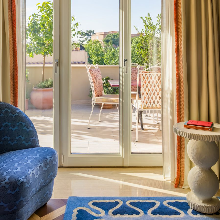 A view of the outdoor terrace on a sunny day viewed through the glass doors inside the bedroom suite of Casa Monti hotel in Rome.