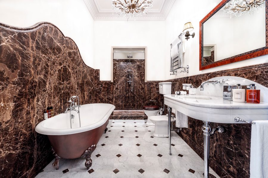 An interior view of the bathroom inside a Hotel Locarno bedroom suite, designed with white and earth tone marble walls.