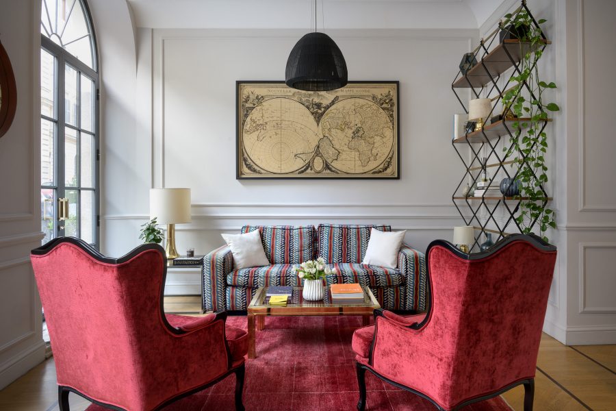 An interior view of a room at The Fifteen Keys, decorated with red lounge chairs and a striped sofa by a tall window.