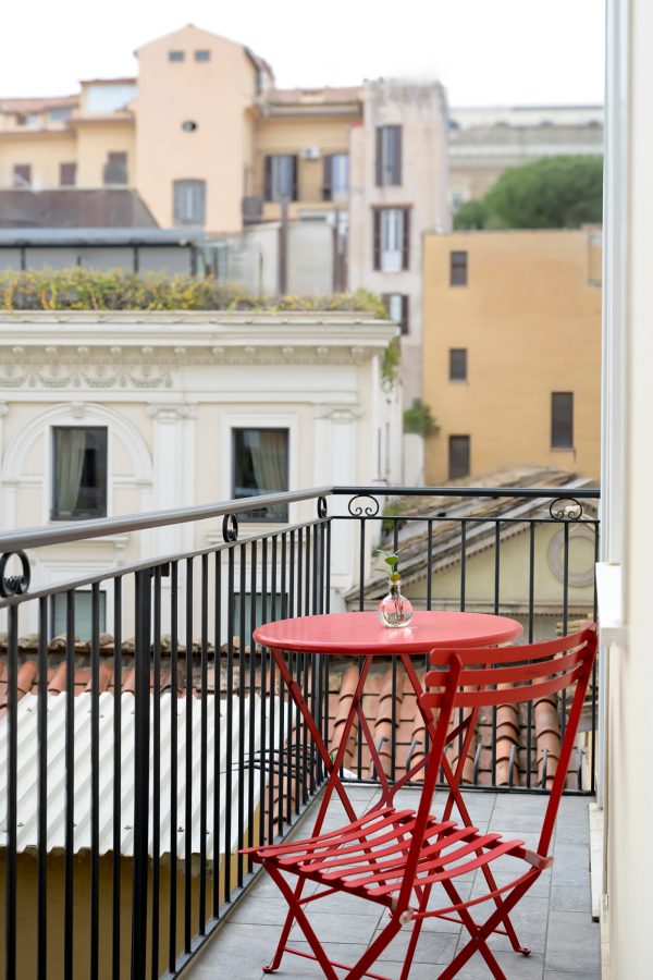 A view of the city and red coffee table and chair on the balcony of a bedroom at The Fifteen Keys in Rome.