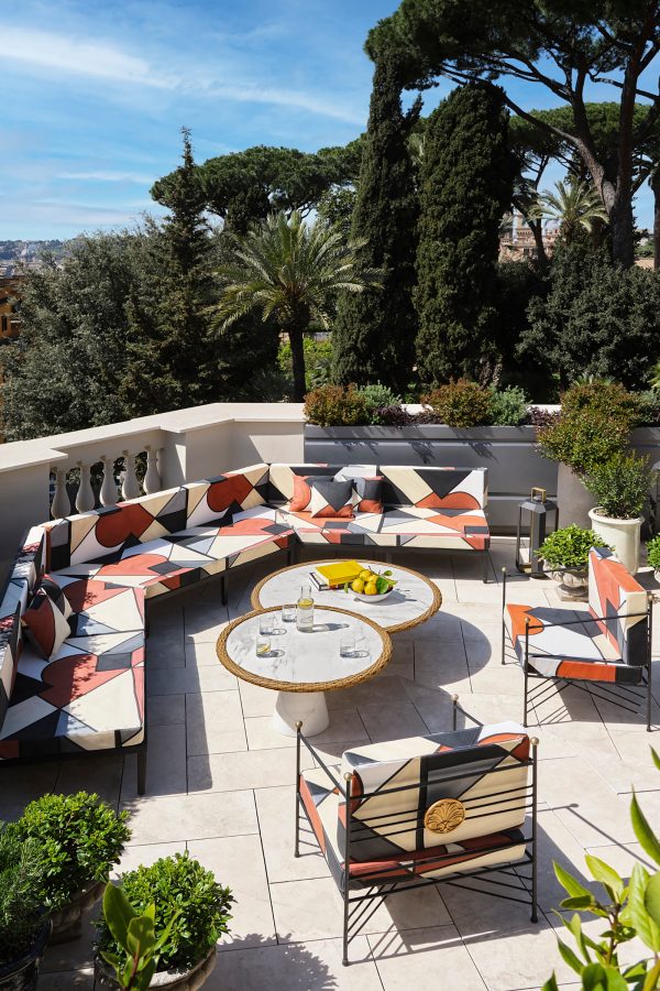 W Hotel Rome rooftop terrace on a sunny day, surrounded by tall trees and decorated with geometric outdoor lounge furniture.