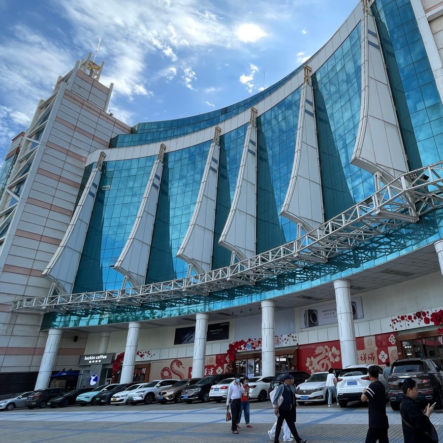 People walk in front of cars parked outside Mingzhu Plaza, a popular area for shopping in Haikou. 