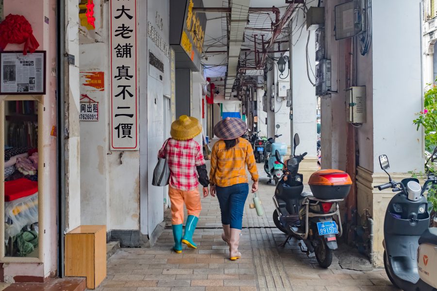 Two people in matching outfits walk beneath a covered pedestrian path along Qilou Old Street in Haikou, Hainan.