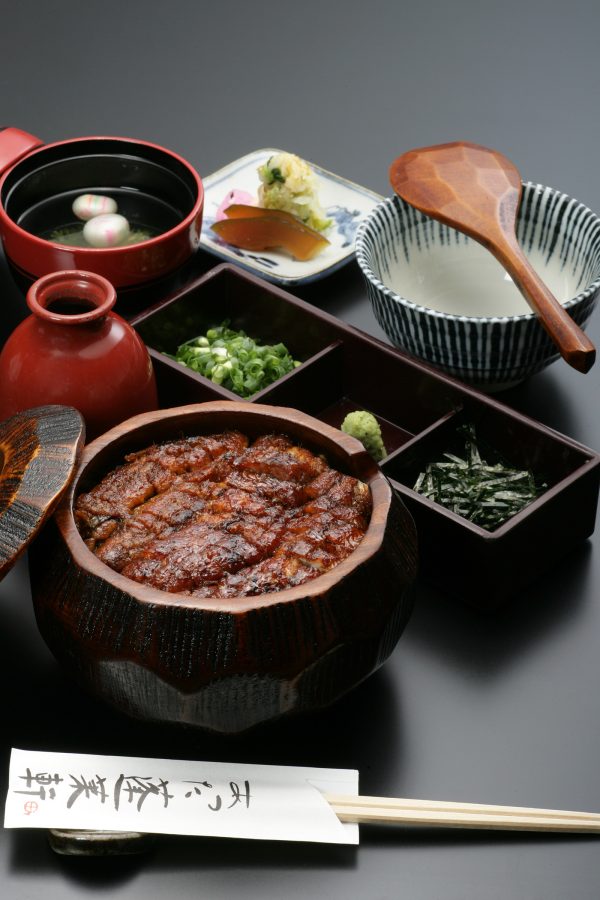  An unagi set from Atsuta Horaiken, which includes grilled eel over rice, side dishes and soup, is spread out across a grey table. 
