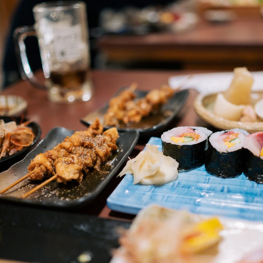 An assortment of dishes found at traditional izakayas like Daijin in Nagoya are spread across a table, including fried skewers and sushi rolls.
