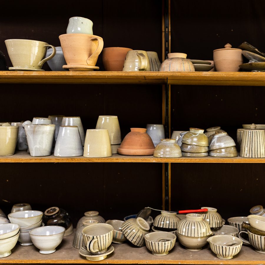Three shelves of ceramics are lined with bowls and cups of various shapes and colours.