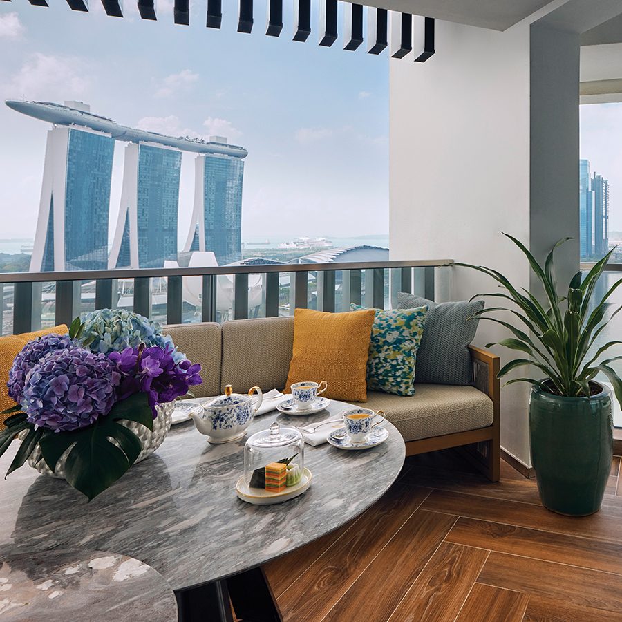 A guest room terrace with a round dining table and couch, offering views of Marina Bay Sands on a clear day.
