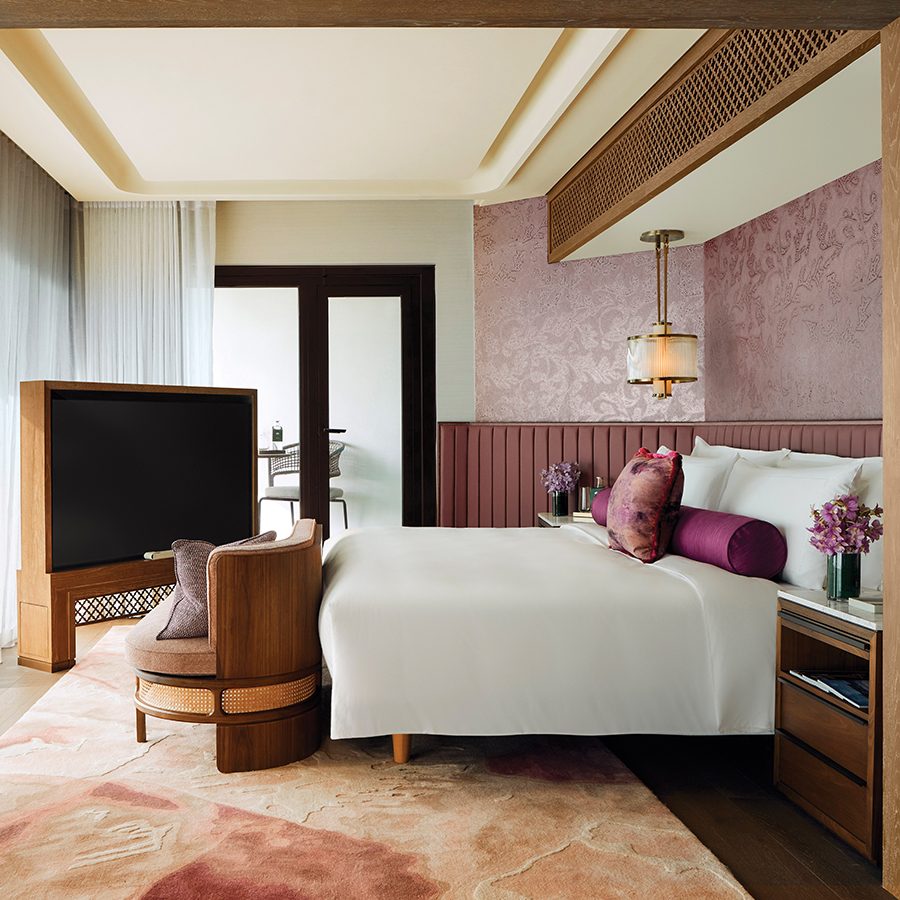 A modern guest room decorated in soft pink and neutral colours, featuring a large bed, couch and free-standing TV.