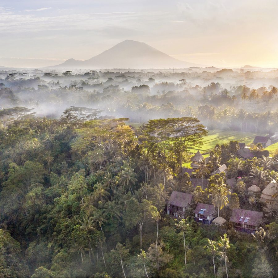 An aerial view over Flying Bamboo Spa, embedded within a tropical forest in Ubud as the sunlight filters through low-lying clouds and the treetops.