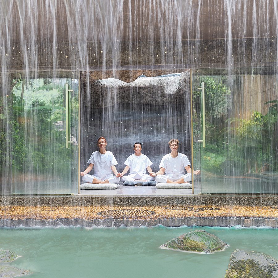 A couple of guests at Mala Spa, Phuket sit cross-legged behind an outdoor rain shower and meditate.