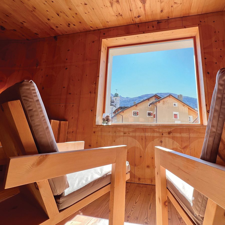 Wooden interiors of the Mineralbad & Spa Samedan, including a window that looks out at the sunny blue sky and surrounding buildings.